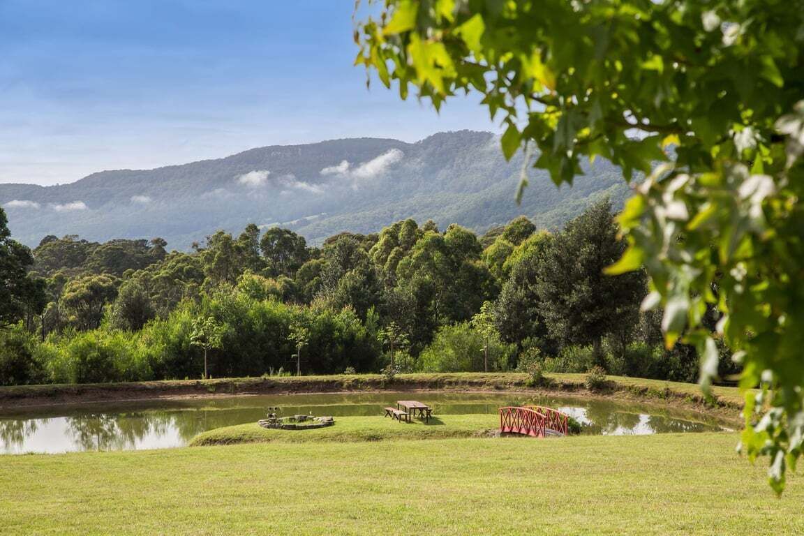 A serene landscape with a pond, picnic tables, and a red bridge.