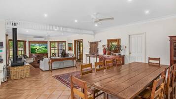 A spacious living area with a wooden dining table, a fireplace, and a large window with a view of greenery.