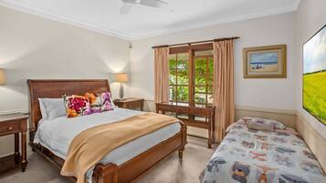 A bedroom with a large bed, a smaller bed, a desk, a chair, a ceiling fan, and a window with curtains.