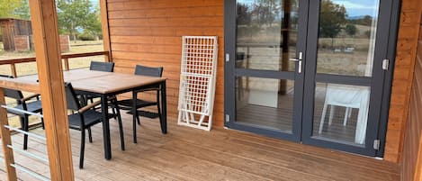 Una terraza de madera con una mesa y sillas, una puerta corrediza de vidrio y vistas al exterior.