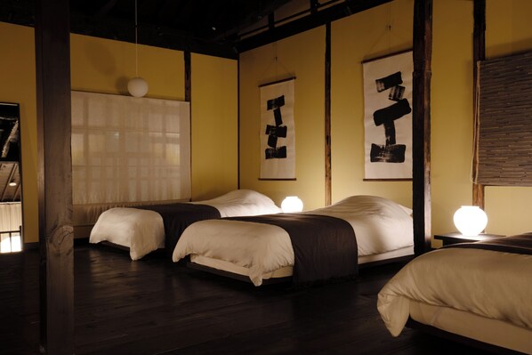 A hotel room with two beds, a wooden floor, and a large window with blinds.