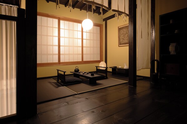 A traditional Japanese room with tatami flooring, a low table with a tea set, a hanging light fixture, and a sliding door.