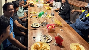 Una larga mesa de madera con personas sentadas a su alrededor, conversando.