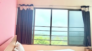Habitación de hotel con una cama grande, una ventana con cortinas y vistas a zonas verdes.