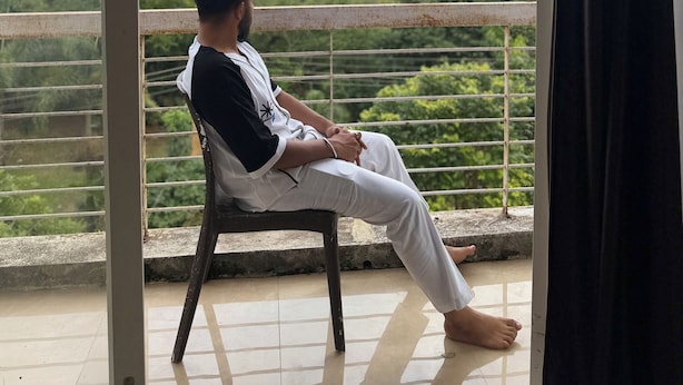 Una persona sentada en una silla junto a una ventana con vistas a un paisaje verde y una presa.