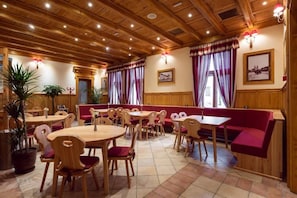 Un restaurante con mesas y sillas de madera, cabinas con cojines rojos y un techo alto de madera con iluminación empotrada.