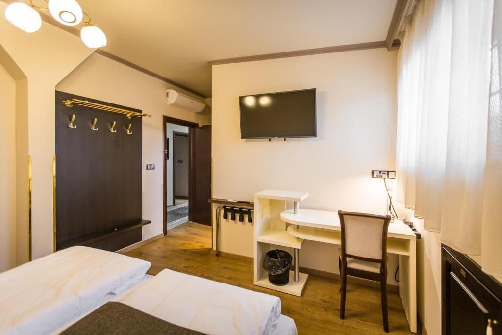 A bedroom with two beds, a desk, a chair, a TV, and a coat rack.
