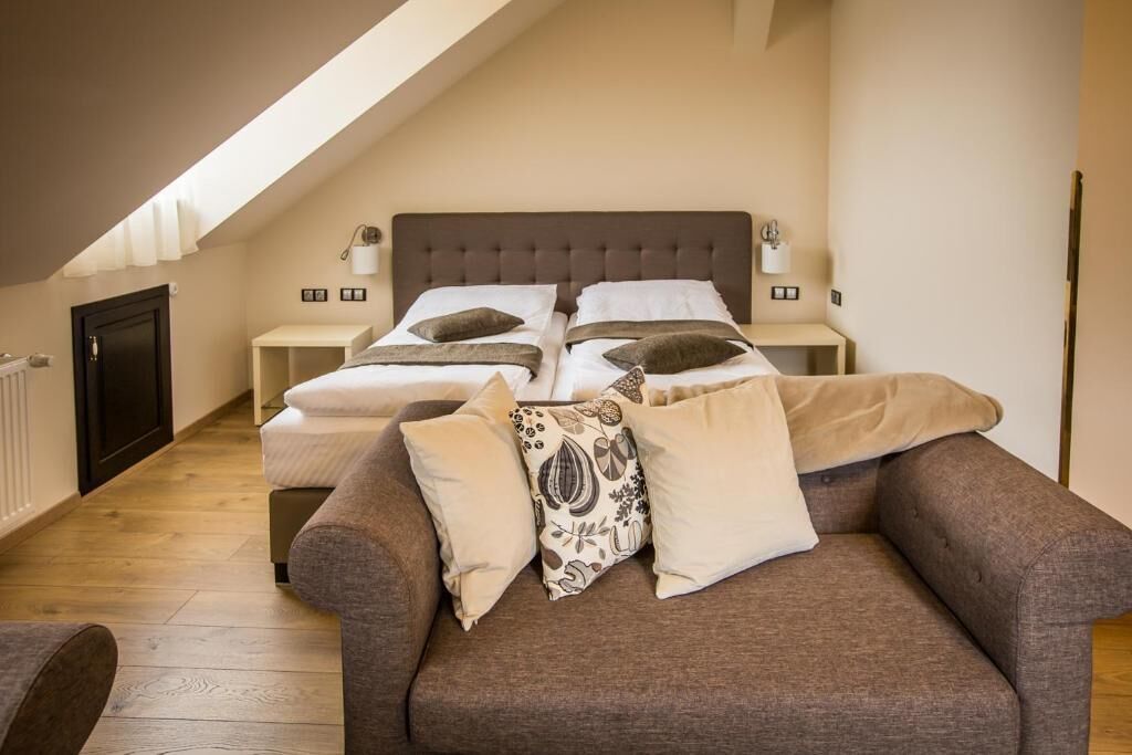 A bedroom with a large bed, two bedside tables, a sofa, and a sloped ceiling with skylight.