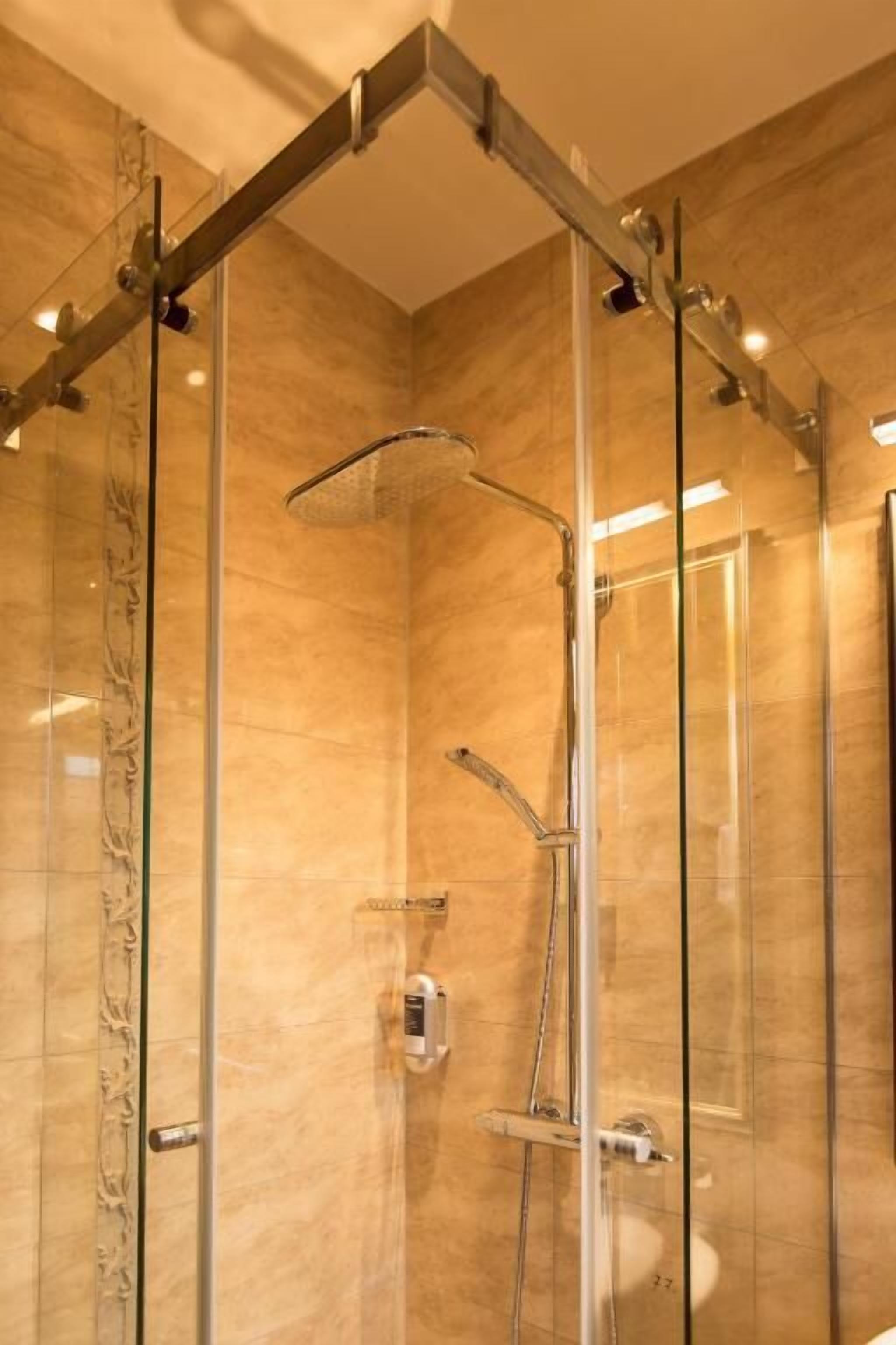 Ducha con cerramiento de vidrio, cabezal de ducha de mano y grifo empotrado.