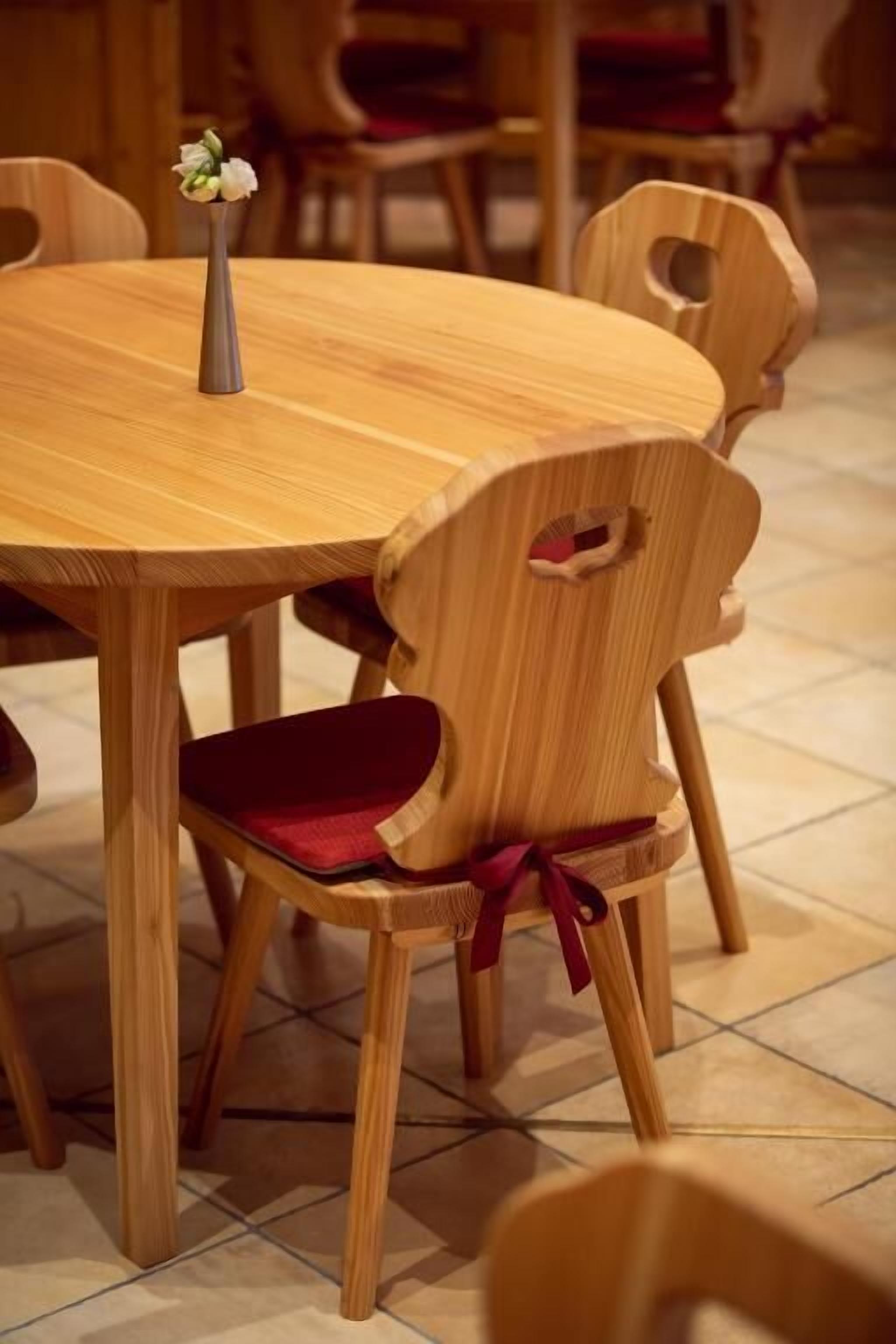 A round wooden dining table with a vase of flowers.