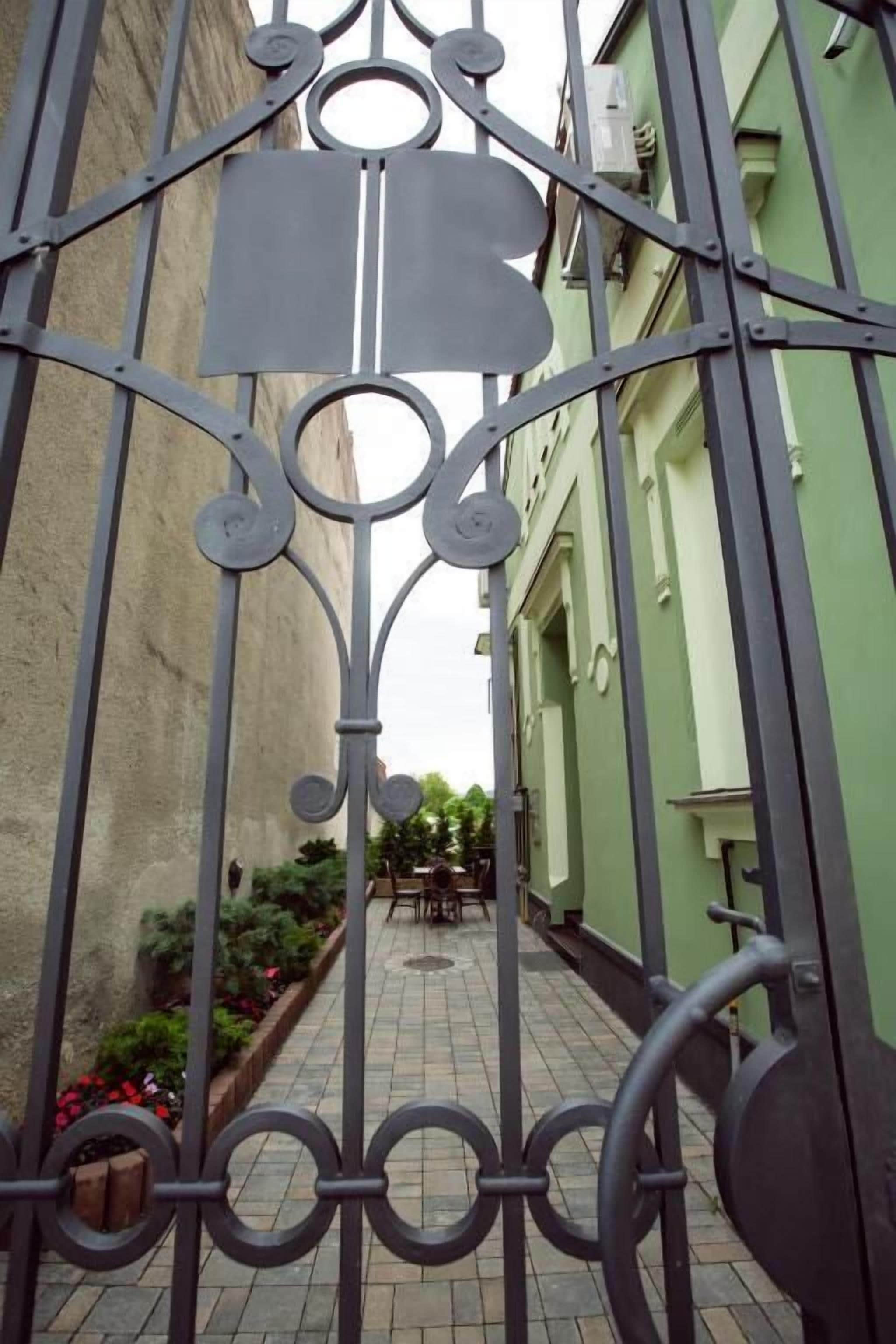 A gated courtyard with a paved walkway, a small table and chairs, and a flower bed.