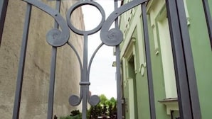 A gated courtyard with a paved walkway, a small table and chairs, and a flower bed.