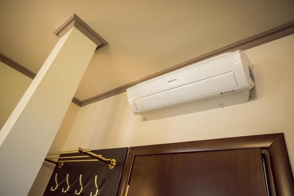 Una habitación con un equipo de aire acondicionado blanco instalado en la pared, una puerta de madera oscura y un perchero metálico negro con ganchos.