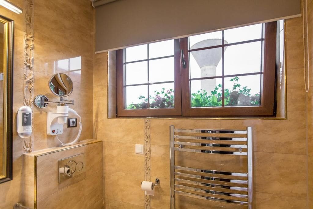 Un bagno con parete in marmo, un porta asciugamani, una finestra vista verde e uno specchio con erogatore di asciugamani.