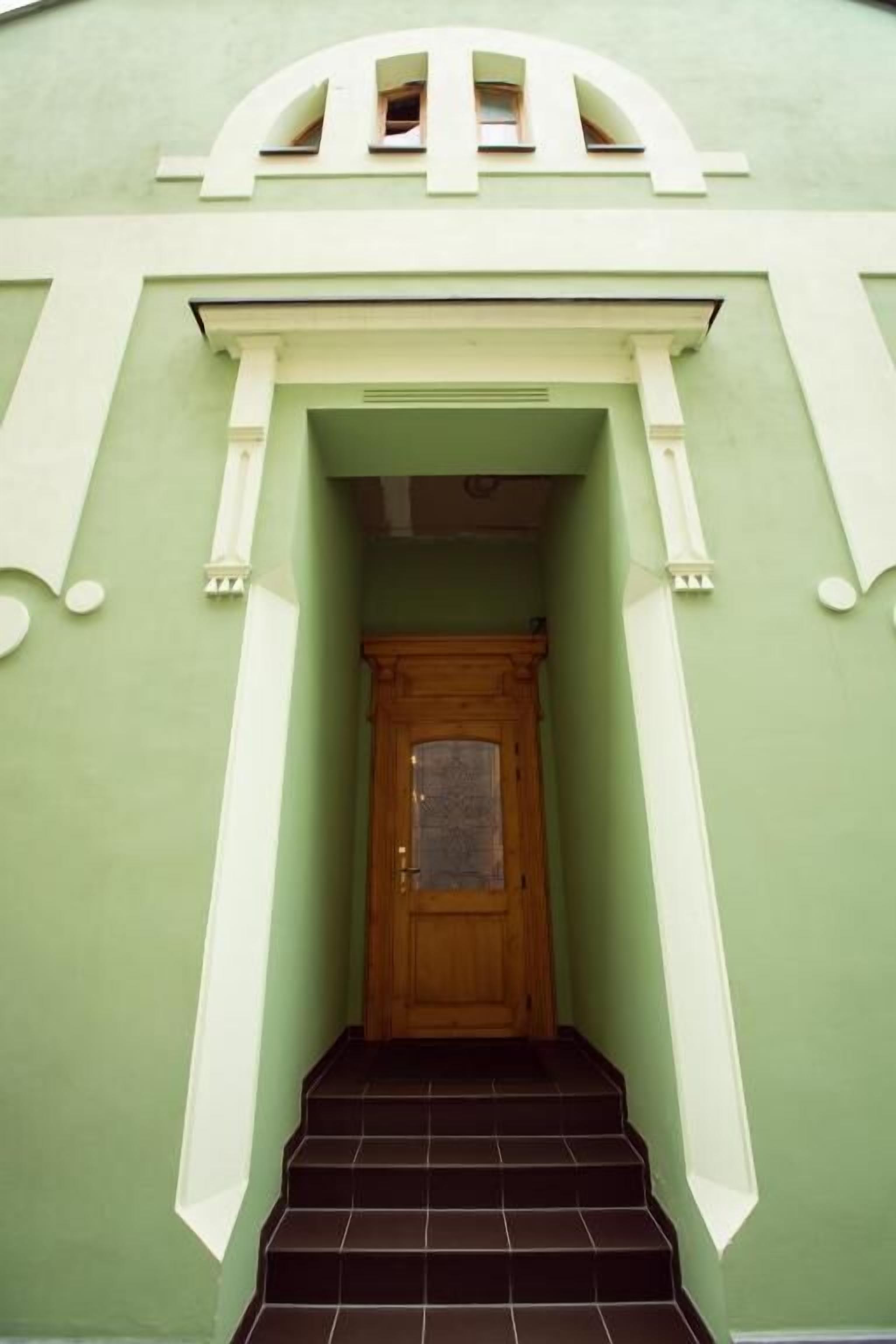A staircase leading to a wooden door with a glass panel, flanked by white columns and a green wall.