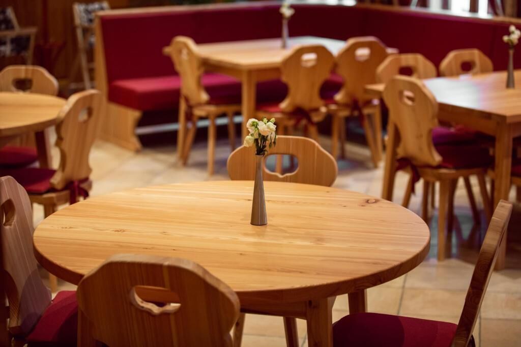 A dining area with round wooden tables and chairs, some with red cushions.