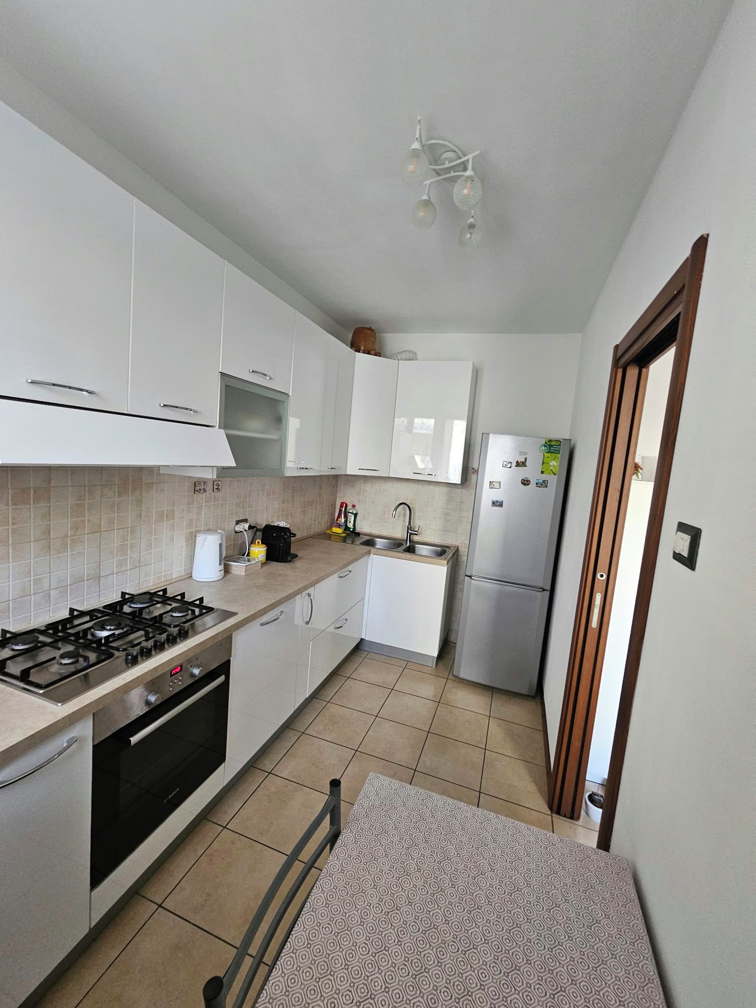 A compact kitchen with white cabinets, a gas stove, a built-in oven, a sink, and a refrigerator.