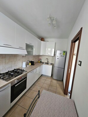 Une cuisine compacte avec des meubles blancs, une cuisinière à gaz, un four encastré, un évier et un réfrigérateur.
