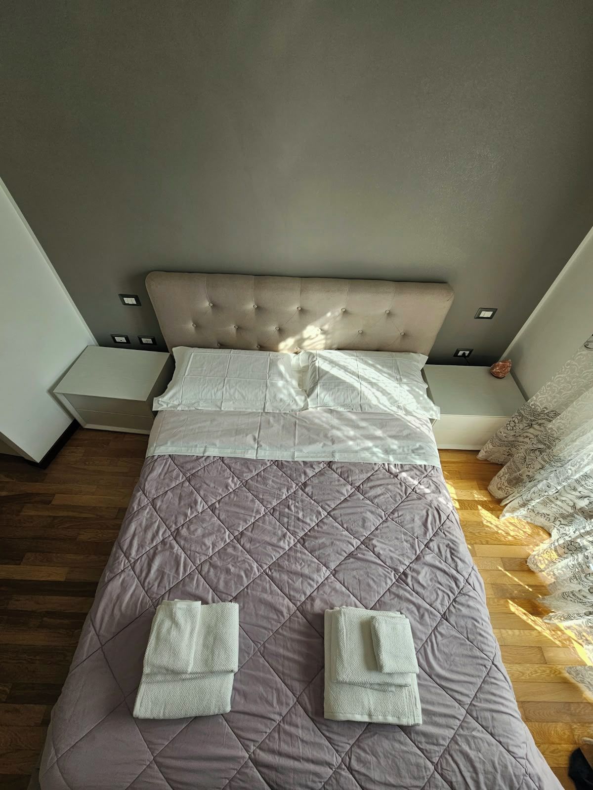 Una cama bien hecha con un cabecero acolchado, dos toallas dobladas y un piso de madera.