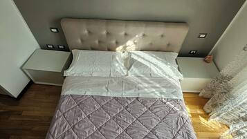 Una cama bien hecha con un cabecero acolchado, dos toallas dobladas y un piso de madera.