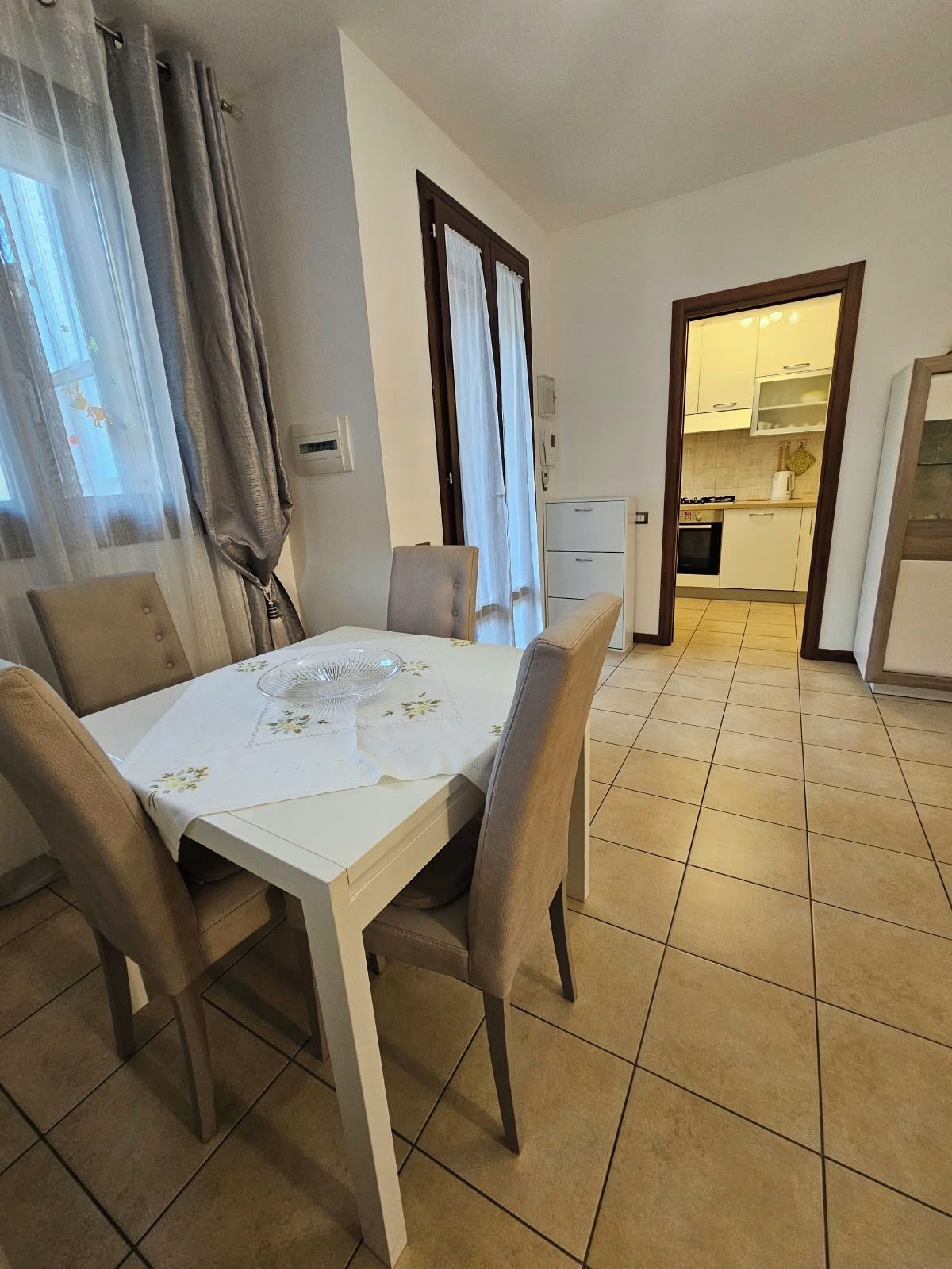 Zona pranzo con tavolo apparecchiato per due, cucina sullo sfondo e una porta che conduce in un'altra stanza.