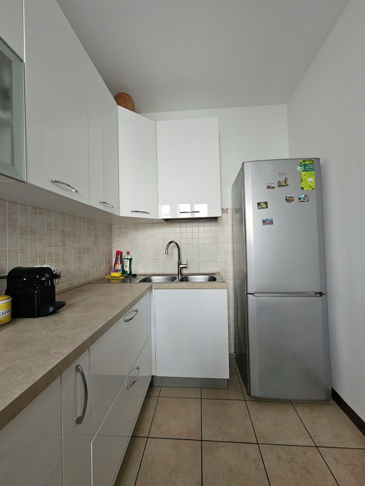 A compact kitchen with white cabinets, a stainless steel refrigerator, a coffee maker, and a sink.