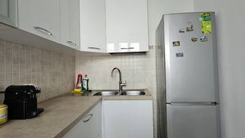 A compact kitchen with white cabinets, a stainless steel refrigerator, a coffee maker, and a sink.