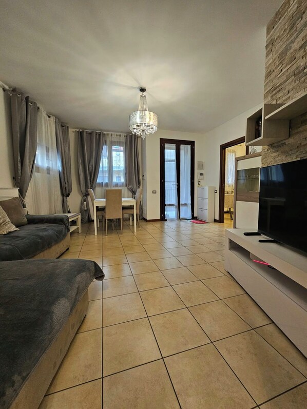A modern living room with a sofa, TV, chandelier, and a dining area with a table and chairs.