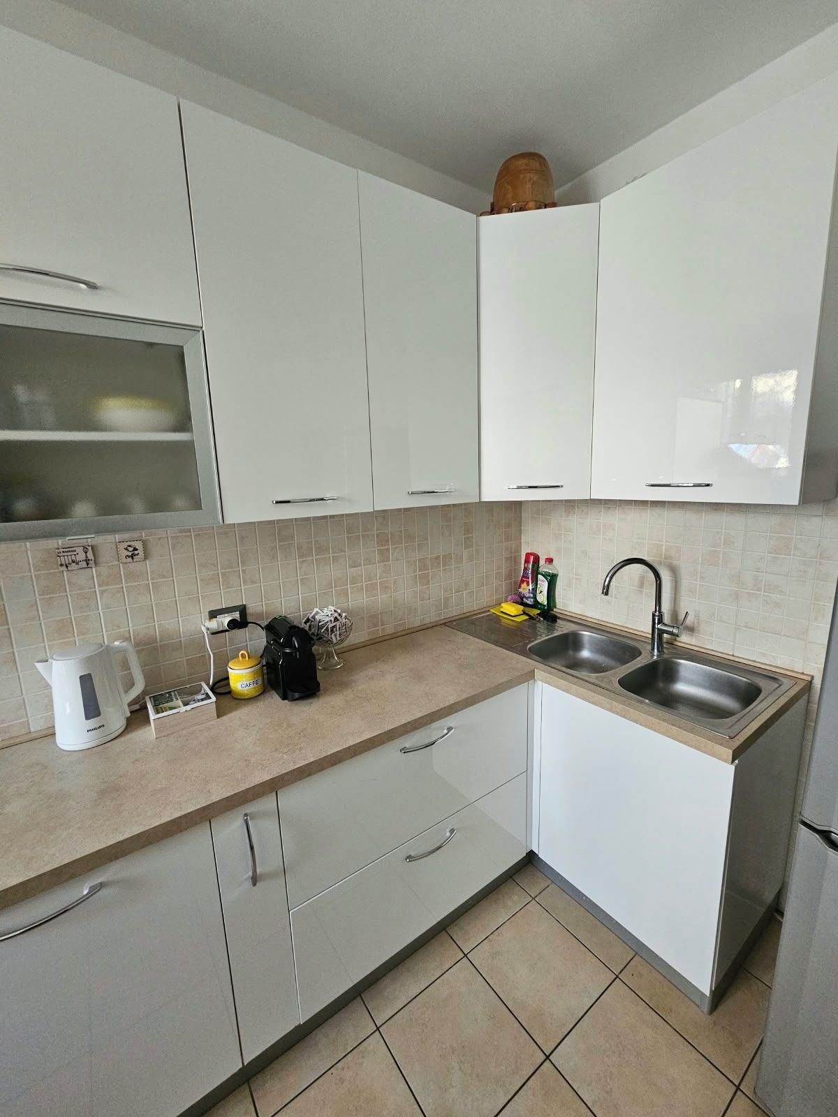 A modern kitchen with white cabinets, a double sink, and a kettle.