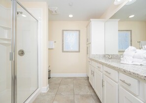 A modern bathroom with a glass shower enclosure, a large mirror, and a marble countertop.
