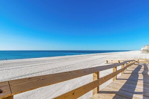 A wooden boardwalk leading to a sandy beach with clear blue skies. - Phoenix Orange Beach 1202 (Orange Beach)