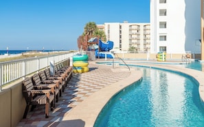 A pool area with a water slide, lounge chairs, and a view of the beach. - Phoenix Orange Beach 1202 (Orange Beach)