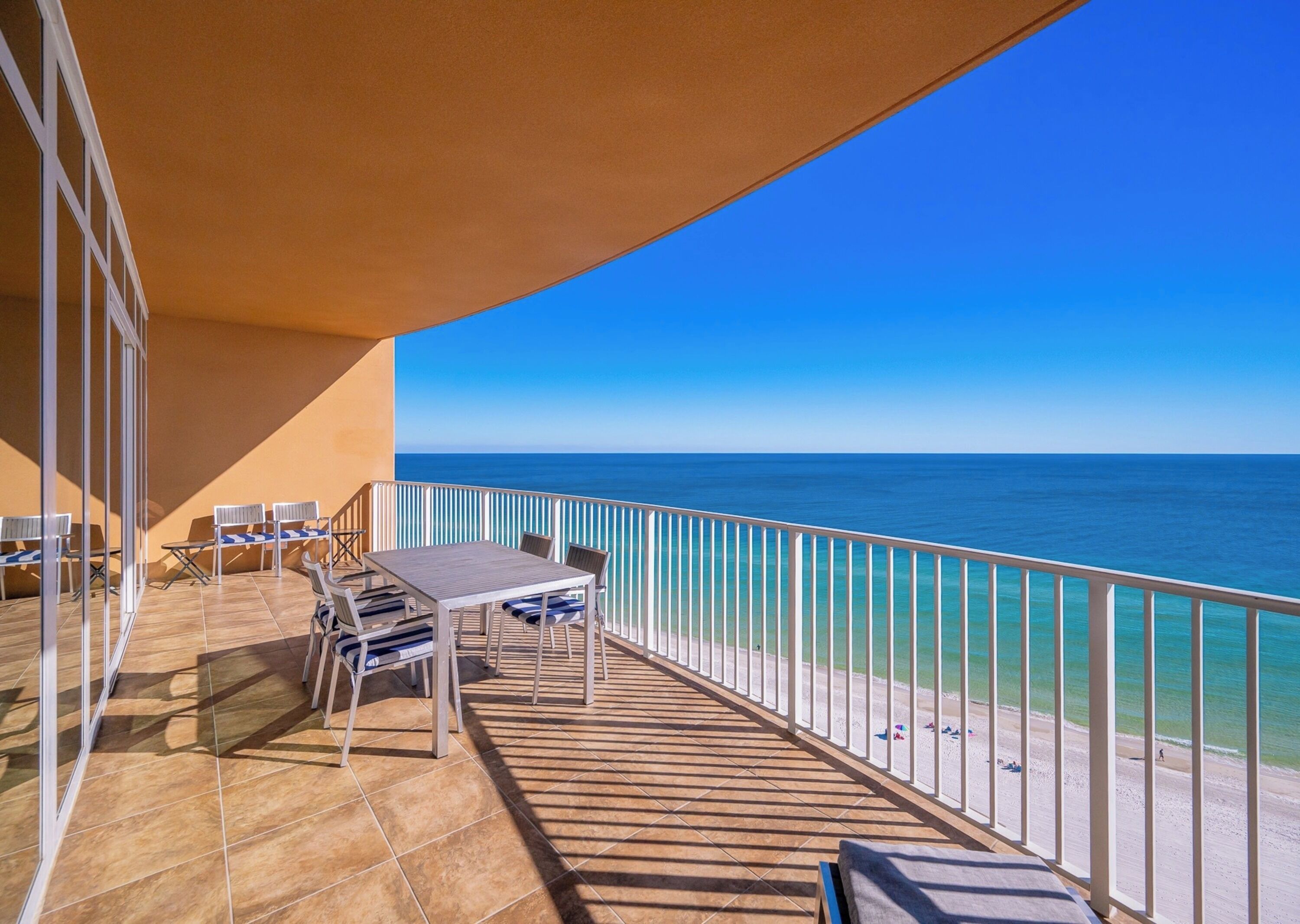 A balcony with a view of the sea, a table, chairs, and a sunshade.