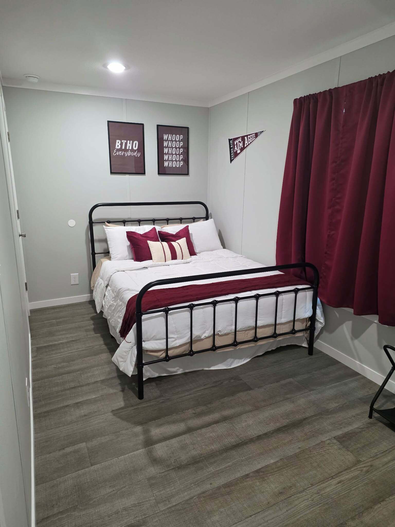 Ein Schlafzimmer mit einem Metallbettgestell, weißer Bettwäsche und einem roten Vorhang.