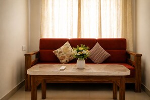 A red sofa with floral cushions and a vase of flowers on a wooden table. - Smiriti Bhawan (Varanasi)