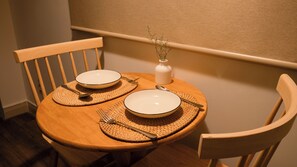 A wooden dining table with two white plates, a white vase with dried flowers, and a woven placemat. - Cozy Studio in Saigon central: D4 Apt by D Haus (Thành phố Hồ Chí Minh)