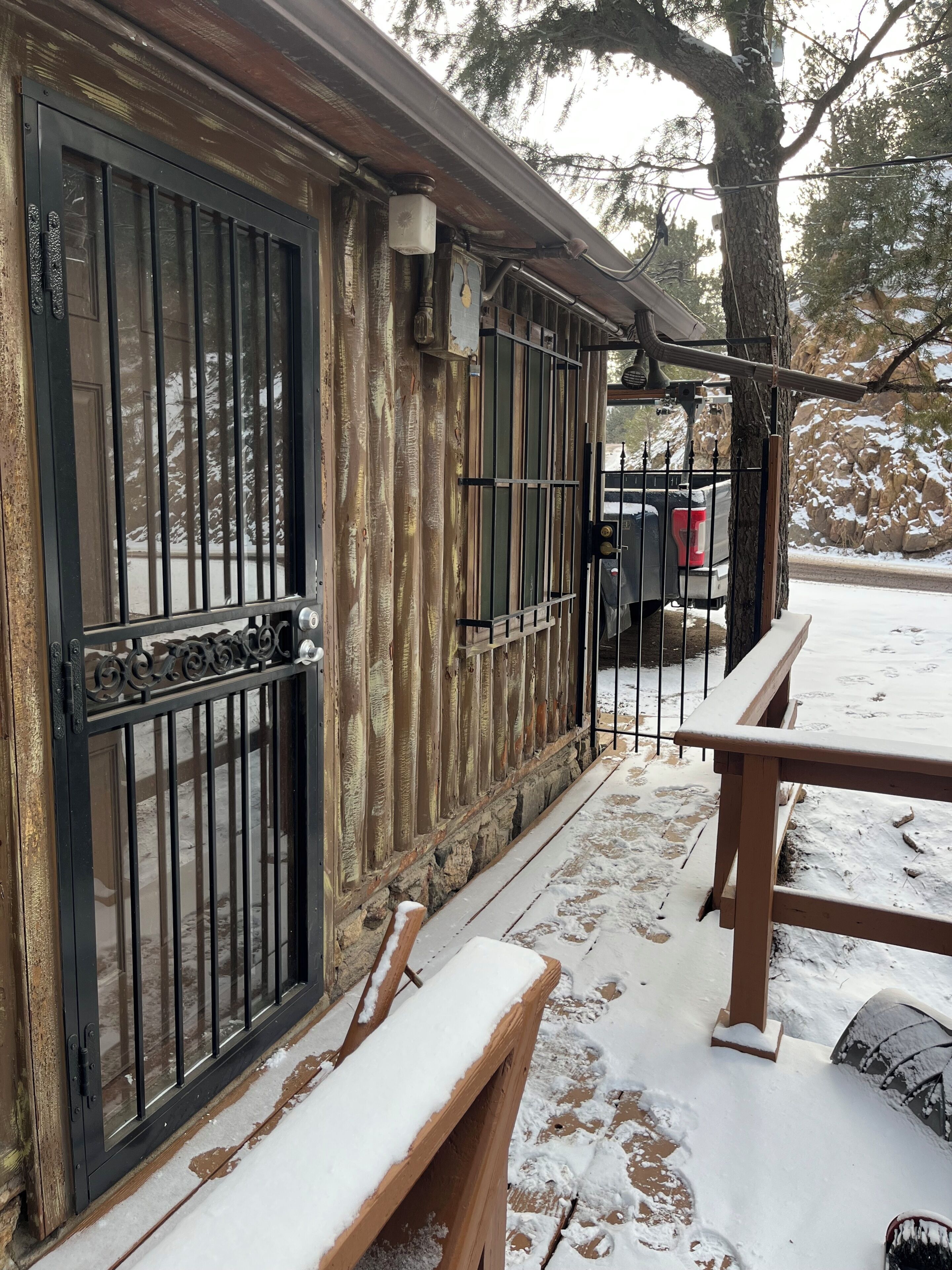 A wooden exterior with a metal gate, a bench, and a parked vehicle.
