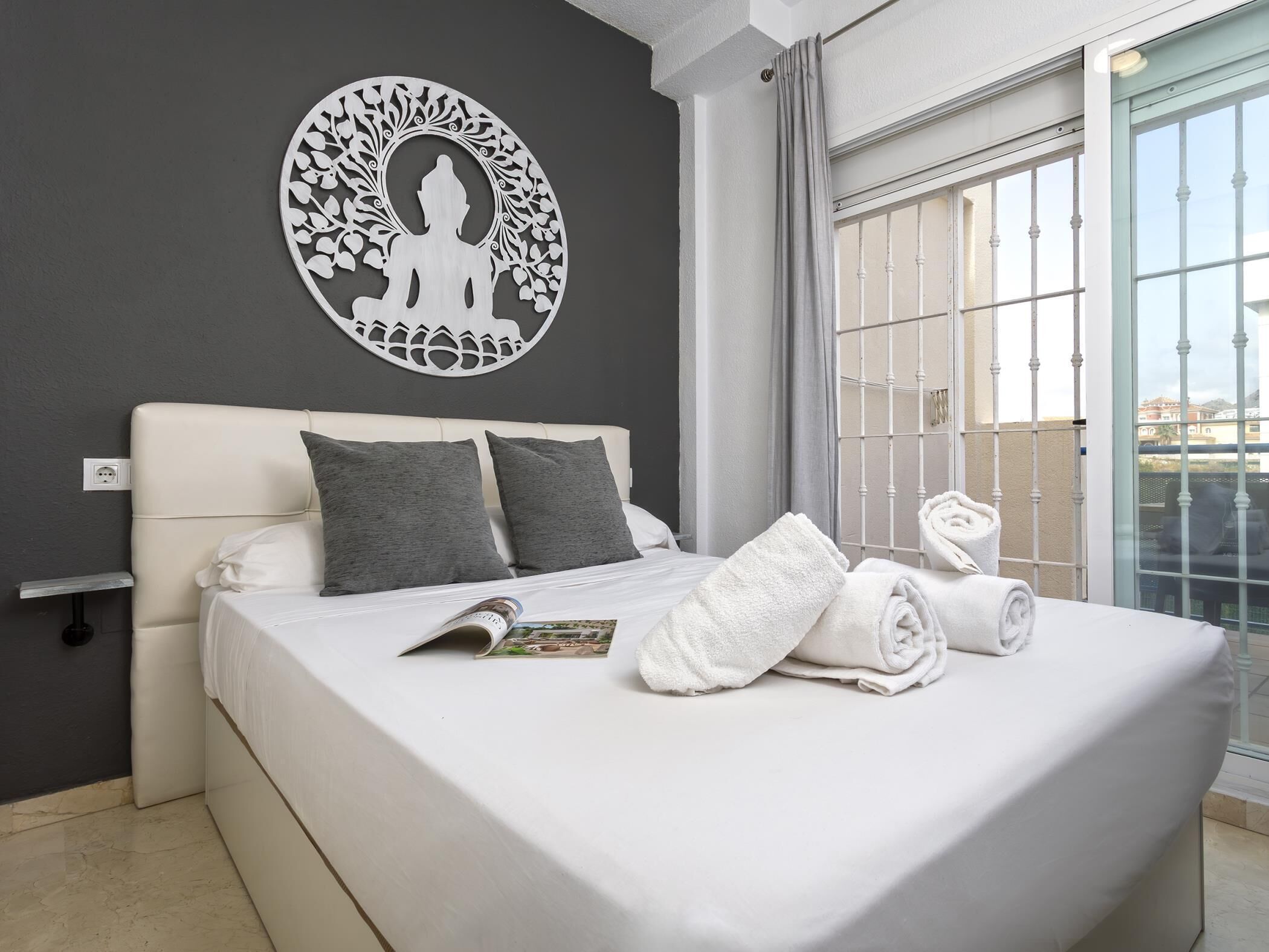 A hotel room with a bed, a wall art piece, a window with a view, and a towel on the bed.