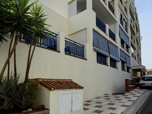 A multi-story building with balconies, a small garden area with palm trees, and a tiled walkway. - Sunstay Flat Torrequebrada (Benalmádena)