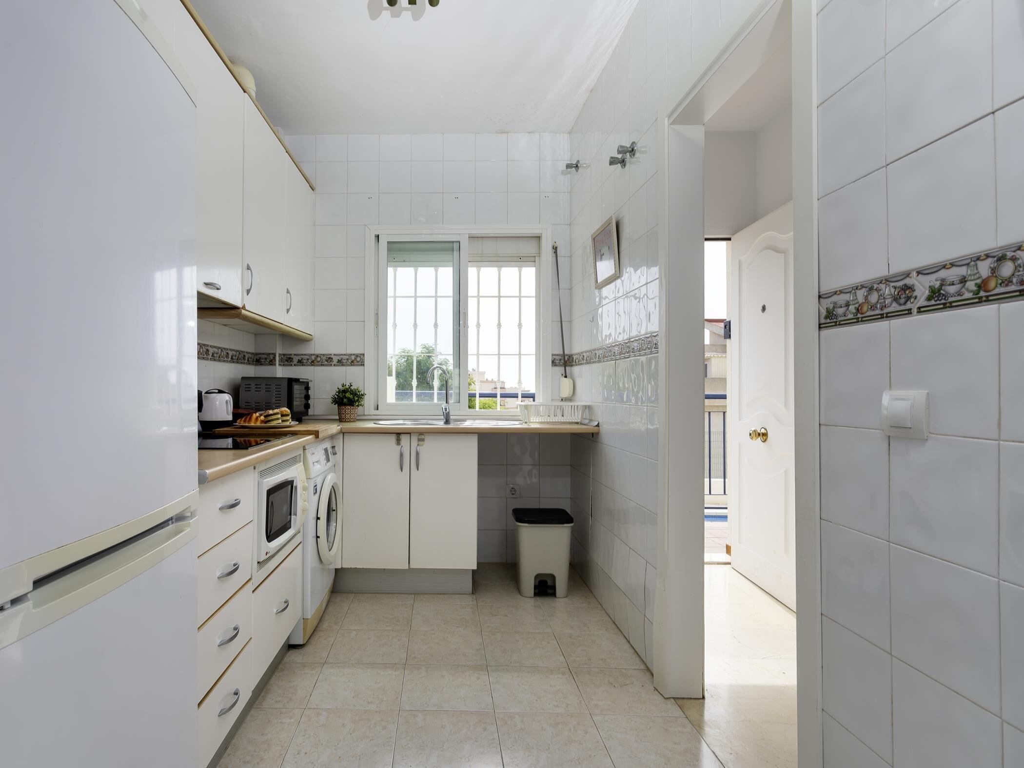 Een smalle keuken met witte kastjes, een magnetron, een oven en een spoelbak.