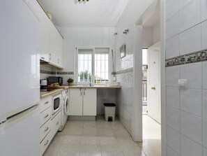 Eine schmale Küche mit weißen Schränken, einer Mikrowelle, einem Backofen und einem Spülbecken.