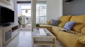 Ein modernes Wohnzimmer mit Flachbildfernseher, einer Couch mit Kissen, einem Couchtisch und einer Pendelleuchte.
