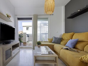 Ein modernes Wohnzimmer mit Flachbildfernseher, einer Couch mit Kissen, einem Couchtisch und einer Pendelleuchte.