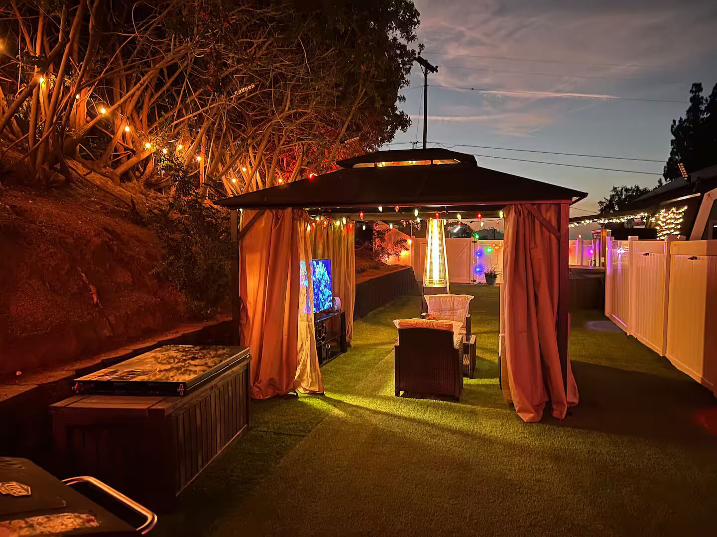 Un espace extérieur aménagé en terrasse, doté d’un coin salon couvert, d’un téléviseur à écran plat et d’un éclairage d’ambiance.