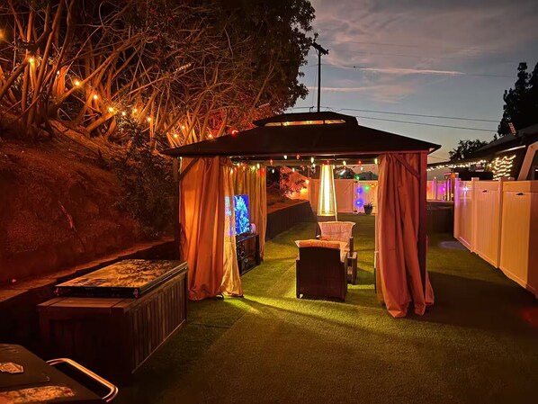 An outdoor patio area with a covered seating area, a flat-screen TV, and ambient lighting.