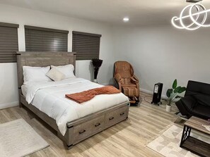 A bedroom with a wooden bed, a massage chair, a black sofa, and a small table.