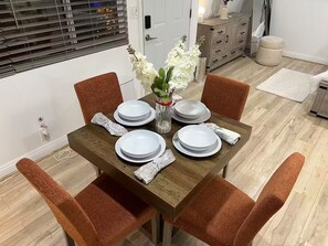 A dining table set with plates and a vase of flowers, surrounded by chairs. - The Manor Cottage (El Cajon)