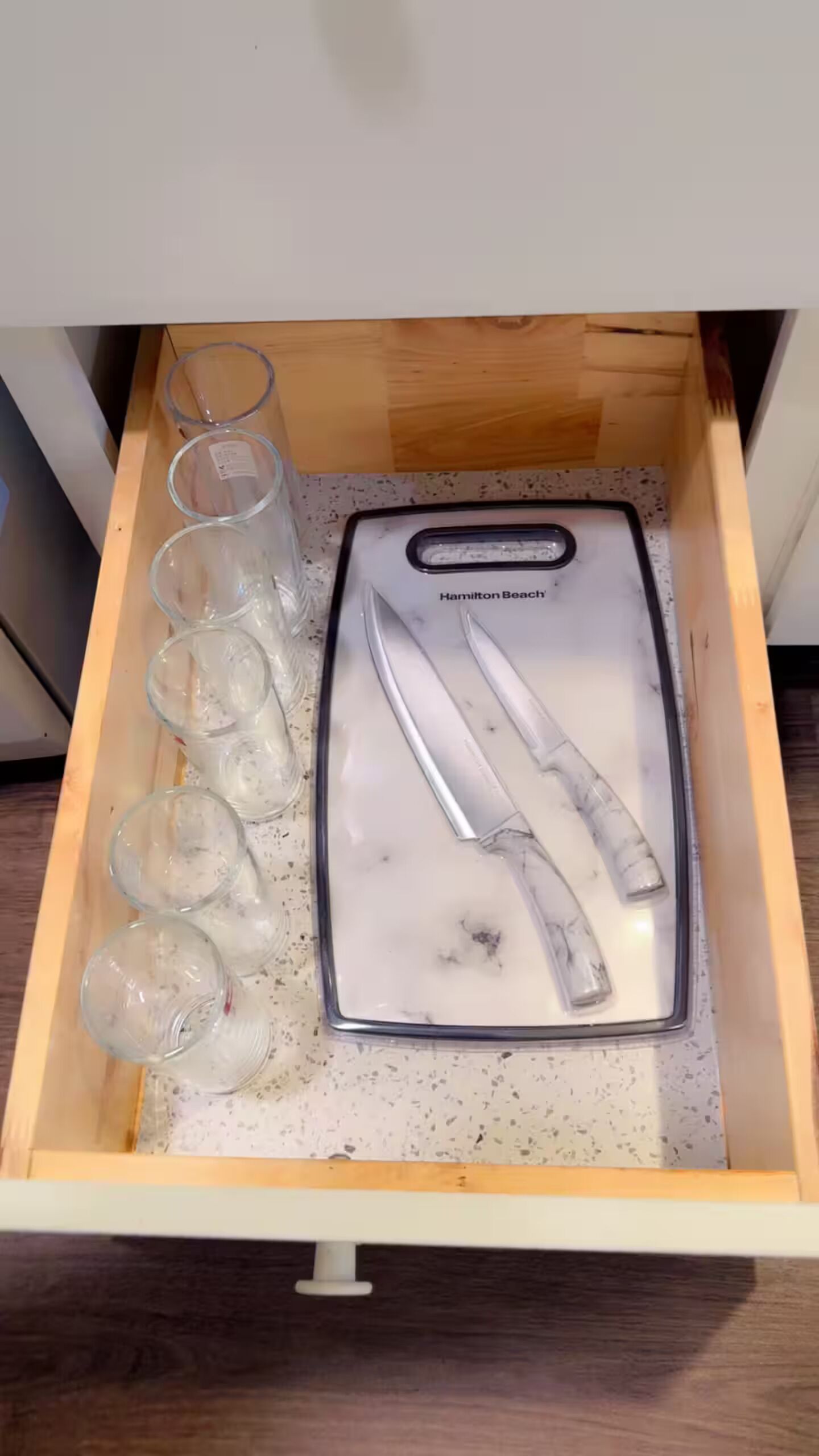 A drawer with a marble countertop, a Hamilton Beach toaster, and six clear glasses.