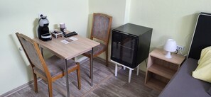 A compact hotel room with a wooden dining table, two chairs, a small refrigerator, a bedside table with a lamp, and a bed with a yellow blanket. - Steakhaus Galgenbach  (Werne)