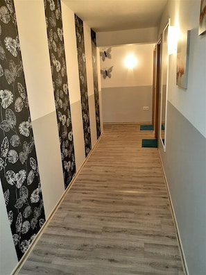 A hallway with patterned wallpaper, wooden flooring, and a light fixture. - Steakhaus Galgenbach  (Werne)